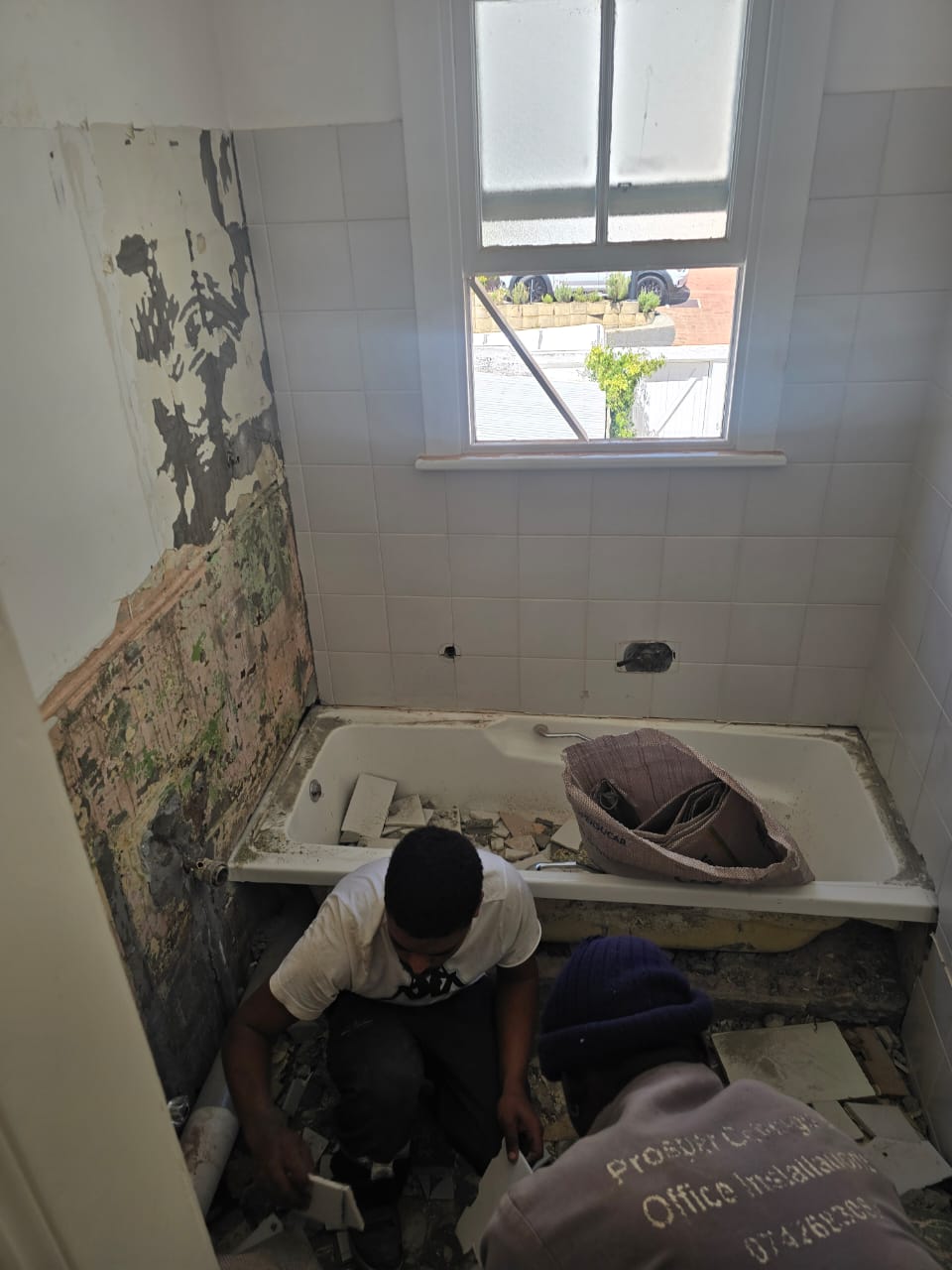 Bathroom strip-out in progress with old tiling and pipework removed